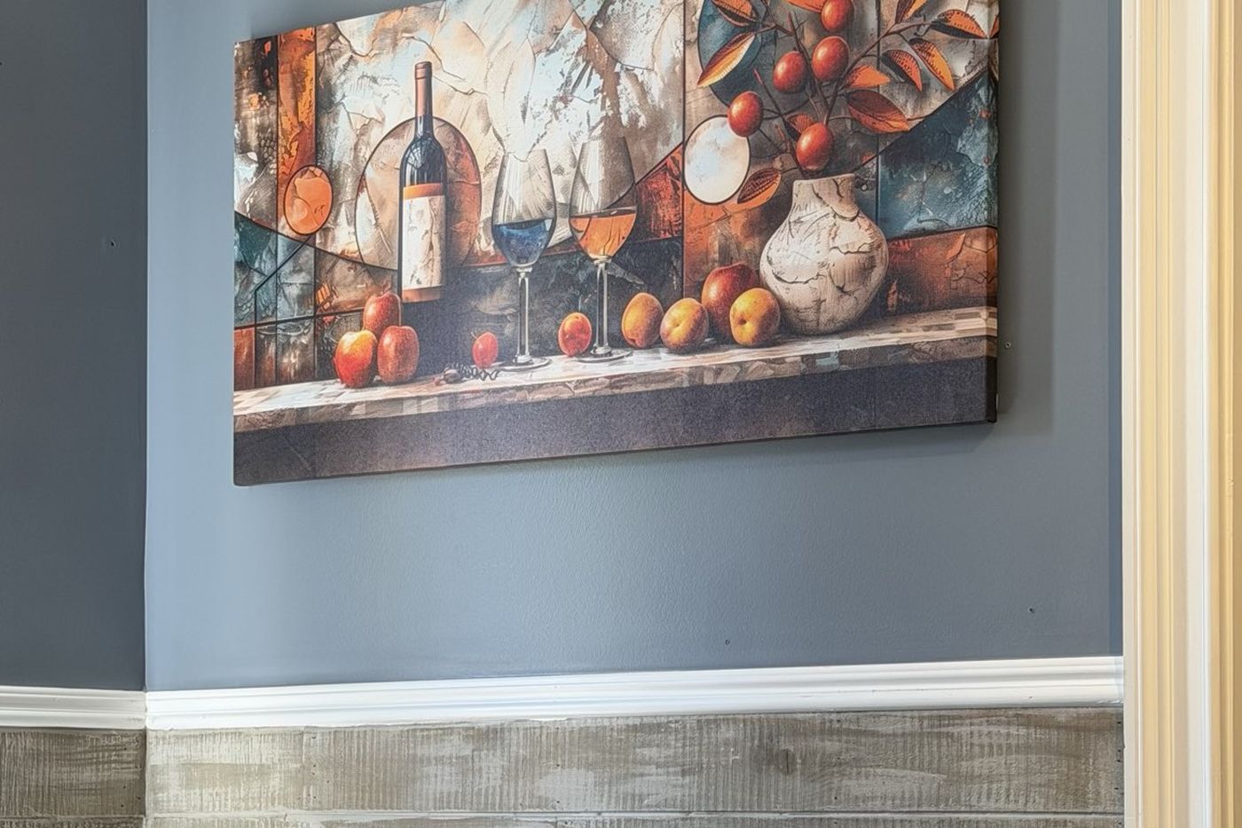 A large still-life canvas of wine and fruit above a two-top table.
