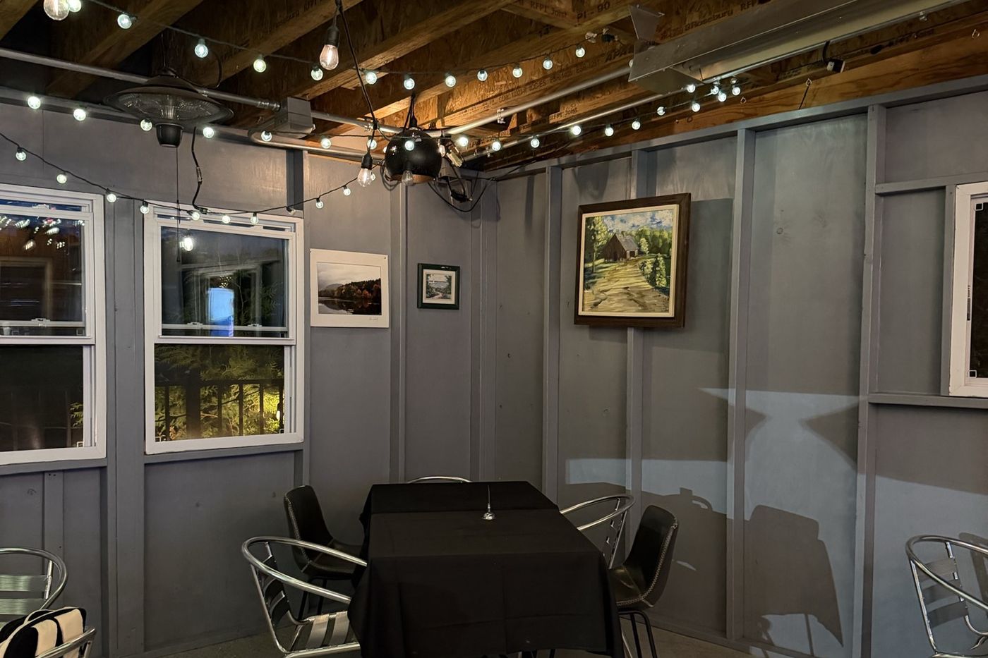 Framed landscape paintings hung along a grey porch wall under string lights.